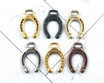 May include: Six metal horseshoe charms in gold, black, silver, and copper finishes. Each charm has a loop for attaching to jewellery or crafts. The horseshoes are arranged in two rows of three.