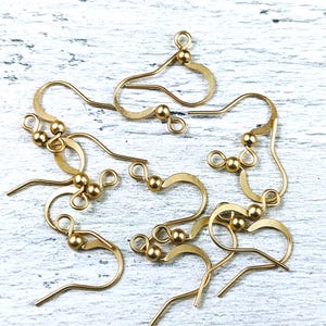 May include: A group of gold-toned earring hooks with small round balls at the top. The hooks are made of metal and are designed for attaching earrings.