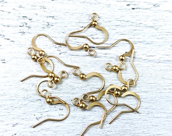 May include: A group of gold-toned earring hooks with small round balls at the top. The hooks are made of metal and are designed for attaching earrings.