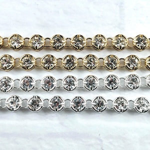 May include: Four parallel rows of rhinestone cup chain, featuring two rows in a gold-tone metal finish and two rows in a silver-tone metal finish. Each row consists of clear, round-cut faceted stones set in individual circular metal settings.