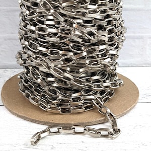 May include: A spool of silver-toned metal chain. The chain is made of flat, oval-shaped links.