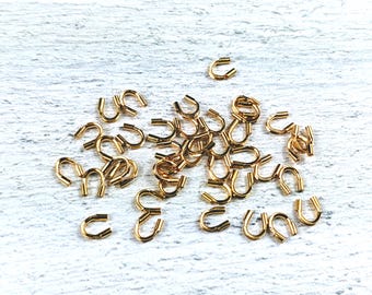 May include: A pile of gold-colored metal jump rings, also known as split rings, used for connecting jewelry components.