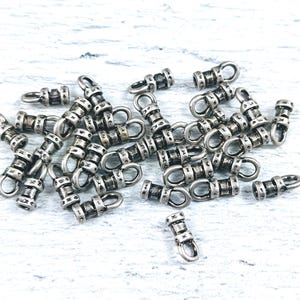 May include: A group of silver-toned metal end caps with a decorative design. The end caps have a loop on one end and a flat surface on the other end.