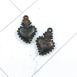 May include: Two antique bronze heart charms with a textured finish. Each charm has a heart shape with a beaded border and a flame design at the top, ideal for jewellery making.