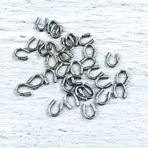 May include: A pile of silver-toned metal crimp end caps for jewelry making.