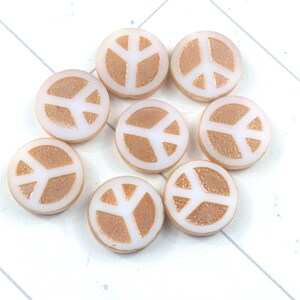May include: A collection of eight round beads with a peace symbol design. The beads have a white background with a copper-colored peace symbol in the center. The beads are scattered on a white surface.