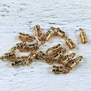 May include: A group of 14 gold-colored metal end caps for cords or straps. The end caps have a decorative design and are used for finishing off cords or straps.