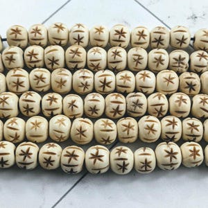 以下が含まれることがあります： オフホワイトの樽型のビーズが並んでおり、それぞれに彫刻されたスターバーストのデザインが施されています。ビーズは紐で繋がれており、繰り返しのパターンを形成しています。これらのビーズは、ジュエリー作りやその他の工芸品に使用される可能性があります。