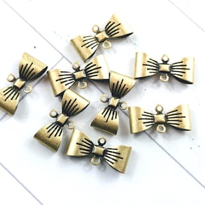 May include: A collection of eight antique gold-toned metal bow tie charms. The charms are designed to be used as embellishments for jewellery making or other craft projects.