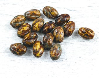 May include: A collection of 15 brown and yellow oval-shaped beads with a marbled pattern. The beads are made of ceramic and have a glossy finish.