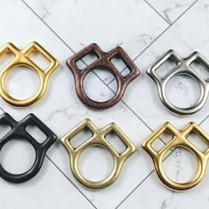 May include: Six metal rings in various colours: gold, bronze, silver, black, antique brass, and another gold. Each ring has a unique shape with a circular centre and a rectangular top.