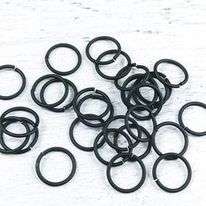 May include: A pile of black jump rings, a type of metal ring used in jewelry making and crafting.