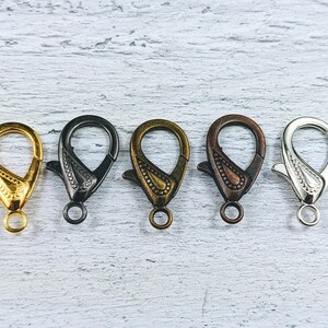 May include: Five metal lobster clasps in different finishes: gold, black, bronze, silver, and antique silver.