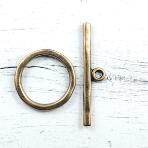 May include: Antique bronze toggle clasp set. The set includes a circular ring and a straight bar with a small loop. The clasp is designed for jewelry making and crafting projects. The metal has a vintage, aged appearance.