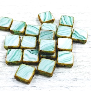 May include: A collection of square glass beads with a marbled design. The beads feature a light blue and white swirl pattern with a brown border. These beads are ideal for jewelry making and crafting projects.