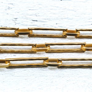 May include: Gold chain with a hammered texture. The chain is made of linked rectangular pieces with rounded edges.