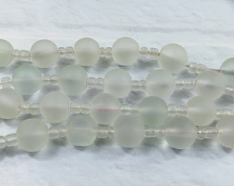 May include: Close-up of three strands of frosted glass beads. Each strand features large, round beads separated by smaller, clear beads. The beads have a soft, translucent appearance, with a subtle, milky white color.