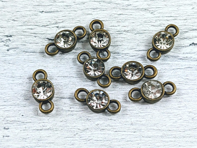 May include: Eight antique bronze connector charms with clear crystal rhinestones. Each charm has two loops for attaching jewelry.