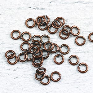 May include: A pile of copper jump rings, a type of jewelry finding, on a white wooden surface.