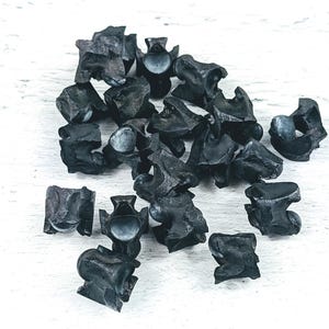 Puede incluir: Un montón de tachuelas de metal negro, algunas con punta puntiaguda y otras con cabeza plana, sobre una superficie de madera blanca.