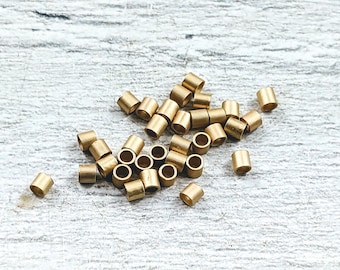 May include: A pile of gold-coloured metal jump rings. The rings are small and round, and they are scattered on a white wooden surface.