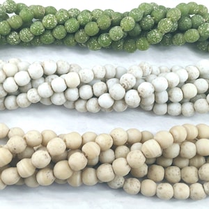 May include: Three strands of round, speckled glass beads. The top strand is green, the middle strand is white, and the bottom strand is beige.