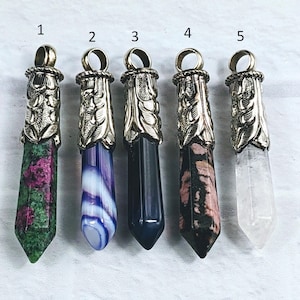 May include: Five silver and crystal pendants with different colored stones. The pendants are numbered 1 through 5. The stones are green, white and blue, black, pink and white, and clear.