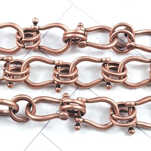 May include: Close-up of three rows of copper-colored chain links. Each link is a unique design, featuring a combination of curved and looped elements. The chains are arranged parallel against a white background with subtle diagonal lines.