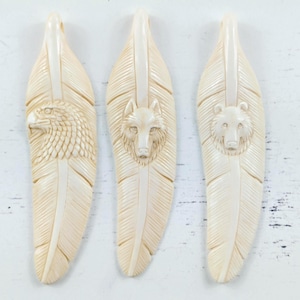 May include: Three off-white, feather-shaped pendants carved from a smooth material. Each pendant features a detailed relief of an animal head: an eagle in profile, a forward-facing wolf, and a forward-facing bear, all set against a textured feather design.