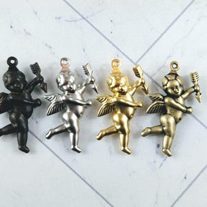 May include: Four metal cupid charms in black, silver, gold, and antique gold finishes. Each charm features a cherubic figure with wings, holding a bow and arrow. Suitable for jewellery making or craft projects.