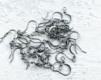 May include: A pile of silver-colored earring hooks, each with a curved hook and a small ball accent. The hooks are scattered on a white, textured surface, suggesting a craft or jewelry-making theme.