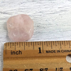 May include: A pale pink rose quartz crystal measuring approximately 2.5 cm in diameter. The crystal is smooth and has a slightly translucent appearance.