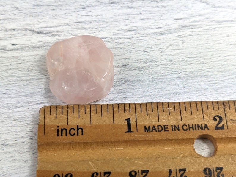May include: A pale pink rose quartz crystal measuring approximately 2.5 cm in diameter. The crystal is smooth and has a slightly translucent appearance.
