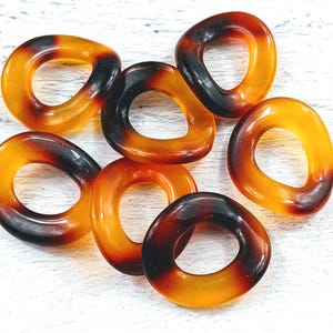 May include: Seven brown and orange plastic rings with a smooth, glossy finish. The rings are all different sizes and shapes, but they all have a similar design.