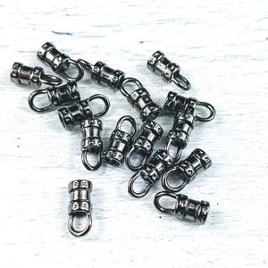 May include: A close-up of a group of black metal cord end caps. The caps have a small loop on one end and a barrel shape on the other end. The caps are used to finish off cords and prevent fraying.