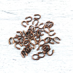 May include: A pile of small, copper-colored metal hooks. The hooks are U-shaped and have a smooth finish.