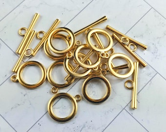 Puede incluir: Una colección de cierres de palanca y anillas de salto de metal dorado. Los cierres tienen forma de barra con un anillo en cada extremo. Las anillas de salto son redondas.