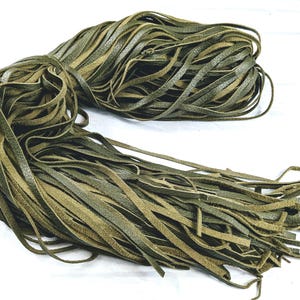 May include: A bundle of green leather cord, approximately 1/4 inch wide, is shown in a loose pile. The cord is made of two layers of leather, one green and one brown, that are sewn together.