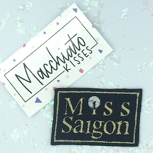 Puede incluir: Un parche bordado en negro y dorado con el texto "Miss Saigon" en letras doradas.