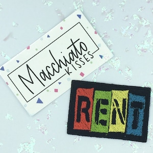 May include: A black fabric patch with the word "RENT" in colourful embroidered letters. The letters are in red, green, yellow, and blue.