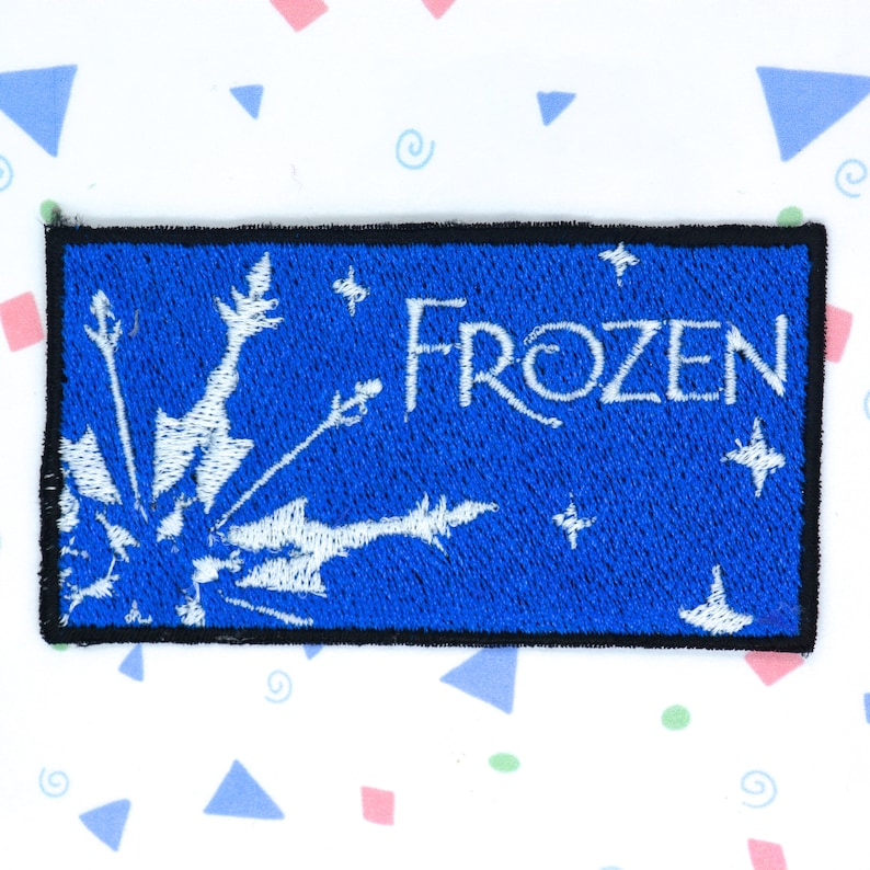 Op de afbeelding: Een blauwe geborduurde patch met een wit sneeuwvlokkenontwerp en het woord "FROZEN" in witte letters.