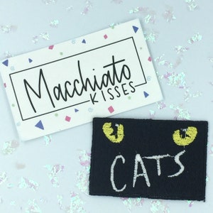 May include: Black felt patch with two yellow cat eyes and the word "CATS" in white embroidery.