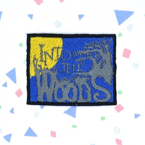 May include: A blue and yellow embroidered patch with the text "Into the Woods" in gray lettering.