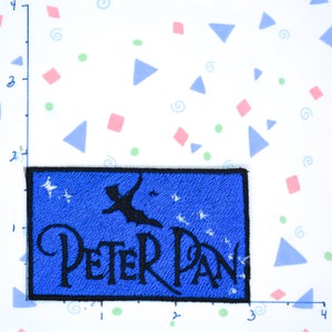 May include: Blue embroidered patch with a silhouette of Peter Pan flying with stars and the text "Peter Pan" in black.