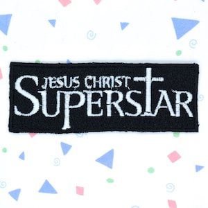 May include: Black embroidered patch with white text that reads "Jesus Christ Superstar" with a white cross.