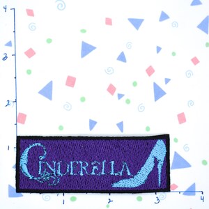 May include: Purple embroidered patch with the word "Cinderella" in blue lettering and a blue glass slipper.
