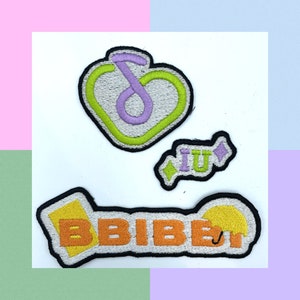 May include: Three embroidered patches with black borders. One is a heart shape with a green outline and a purple musical note. Another patch has the letters "iu" in purple. The third patch has the letters "BBIBI" in orange with a yellow umbrella.