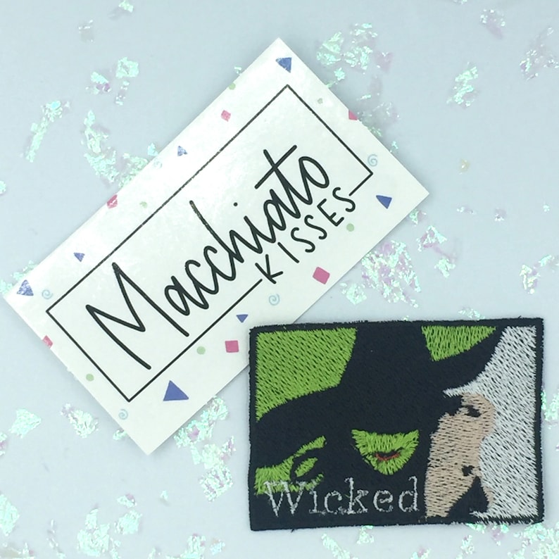 May include: Green and black embroidered iron-on patch featuring a close-up of the Wicked Witch of the West from the musical Wicked. The text "Wicked" is embroidered in white below the image.