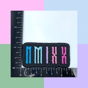 Puede incluir: Un parche bordado negro con la palabra "MIX" en letras de colores. Las letras son azules, azul claro, moradas y rosas.