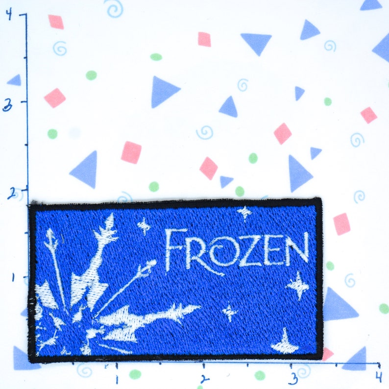 Op de afbeelding: Een blauwe en witte geborduurde patch met het woord "FROZEN" in witte letters. De patch heeft een sneeuwvlokontwerp.